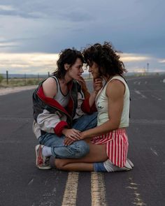 two people sitting on the ground next to each other and one is holding something in his mouth