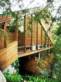 a wooden house with stairs going up to it's second story and trees growing on the other side