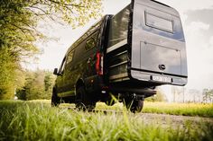 a black van parked on the side of a road near some tall grass and trees