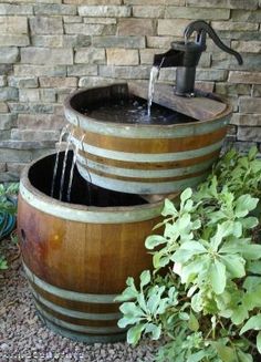 two wooden barrels with water running from them in front of a brick wall and green plants