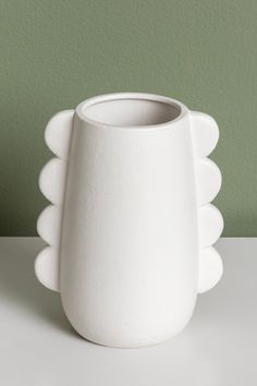 a white vase sitting on top of a table next to a green wall in the background