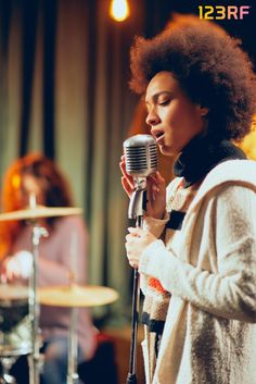 a woman singing into a microphone while standing in front of a drum set and another person behind her