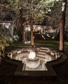 a fire pit in the middle of a yard at night with lights on and trees around it