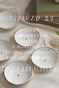 four white dishes with gold rims sitting on a table next to flowers and books