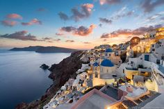 the sun is setting over an island with white buildings and blue domes