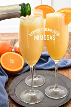 two champagne flutes with orange slices in them on a tray next to an orange and wine bottle