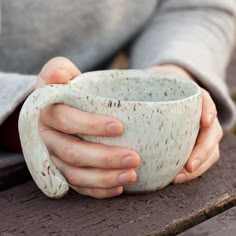 a person holding a white cup on top of a wooden table