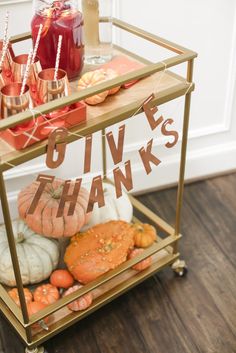 a gold serving cart filled with drinks and pumpkins on top of a hard wood floor