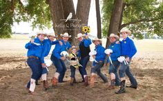 a group of people in blue shirts and cowboy hats posing for a photo under a tree