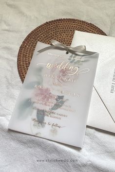 a wedding card and envelope sitting on a white bed sheet next to a wicker basket