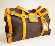 "An authentic Prada shoulder bag. The bag features a brown canvas exterior, orange leather trim, and silver-tone hardware. The interior is lined with yellow leather and there is one zipped pocket. The interior is neat & clean. The exterior is in very good condition, the trim has minor signs of use on the bottom and corners of the bag. Overall the bag is in really good condition and comes with its Prada cards and dust bag. Dimensions (cm & inch) Width: 40 cm / 15,7\" Height: 23,5 cm / 9,3\" Depth Designer Yellow Satchel For Travel, Yellow Travel Shoulder Bag With Palladium Hardware, Yellow Bags With Silver-tone Hardware For Everyday Use, Orange Travel Bag With Silver-tone Hardware, Cognac Travel Bag With Silver-tone Hardware, Yellow Rectangular Bag With Silver-tone Hardware, Brown Satchel With Silver-tone Hardware For Travel, Brown Coated Canvas Shoulder Bag With Palladium Hardware, Brown Travel Bags With Silver-tone Hardware