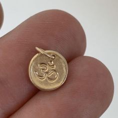 A tiny pendant with a texture like stone and an om or ohm symbol. The pendant measures about a quarter of an inch or slightly larger and is made of solid 14k yellow gold. Also available without the om symbol. A plain pebble pendant is shown modeled on a 16" chain for size reference; chain is not included. Made to order within 3-5 days.See here for more photos: http://www.etsy.com/listing/34030666/tiny-14k-gold-pebble-necklaceIMPORTANT: Please be aware that delivery times are estimates and USPS m Spiritual 14k Gold Charm Necklace With Round Pendant, 14k Gold Spiritual Round Pendant Charm Necklace, Yellow Gold Spiritual Charm Necklace With Moon Charm, 14k Gold Symbolic Charm Necklace With Round Pendant, Symbolic Yellow Gold Brass Charms, Spiritual 14k Gold Charms, Symbolic Engraved Yellow Gold Charms, Spiritual 14k Gold Charm Necklaces With Coin Pendant, Symbolic Yellow Gold Charms With Round Pendant