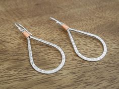 two pairs of silver and copper tear shaped earrings on a wooden table with wood grained surface