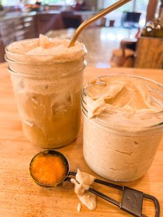 two jars filled with food sitting on top of a wooden table next to a spoon