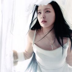 a woman with long black hair wearing a white dress and holding her hand up to the side