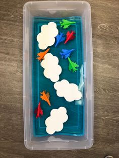 a plastic container filled with paper cutouts and clouds on top of a wooden table