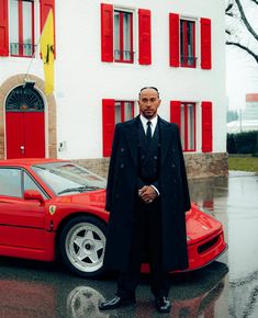 a man standing next to a red sports car in front of a white and red house