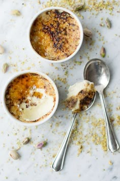 two bowls filled with dessert sitting on top of a white counter next to spoons