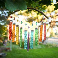 a colorful wind chime hanging from a tree in the grass with beads on it