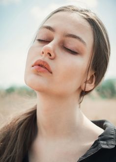 a woman with her eyes closed is standing in front of the sky and looking up