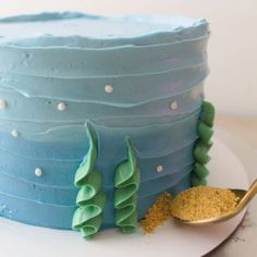 a blue frosted cake on a white plate with a gold spoon next to it