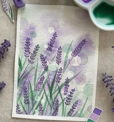 some purple flowers are sitting on a table next to watercolor paints and paintbrushes