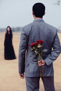 a man in a gray suit holding a red rose and standing next to a woman