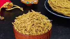 yellow noodles are in a wooden bowl on a black table next to two plates with red napkins