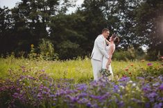 a bride and groom standing in a field with wildflowers