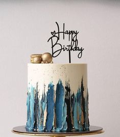 a birthday cake decorated with blue and white icing, gold decorations and a happy birthday topper