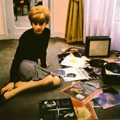 a young boy sitting on the floor surrounded by records and cds, with his legs crossed