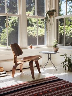 an eames chair in front of a window with potted plants on the floor