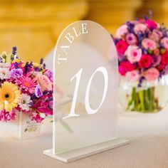 a table number with flowers in vases on top of the table and an acrylic sign that says table 10