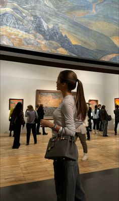 a woman standing in front of a painting holding a gray purse and looking at it