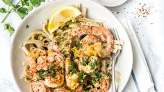 pasta with shrimp and parsley on white plate next to lemon wedges, garnished with parsley