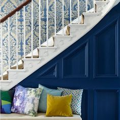 a white staircase with blue walls and colorful pillows on the bench in front of it