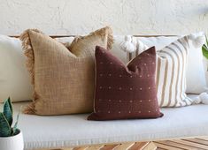 three pillows on a bench next to a potted plant