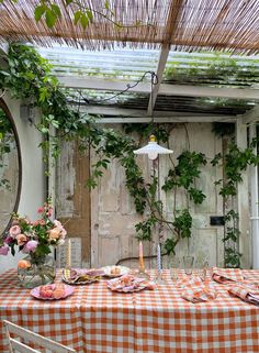 the table is set with an orange and white checkered cloth on it, surrounded by greenery