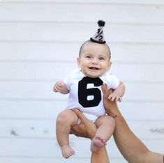 a person holding a baby wearing a black and white number 6 shirt with a party hat on