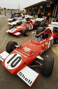 several race cars lined up in front of a building with people looking at them from the side