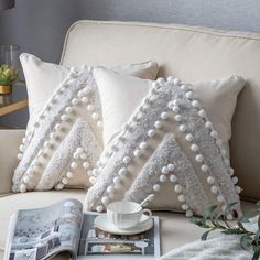 two white pillows sitting on top of a couch next to a cup and saucer