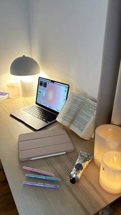 an open laptop computer sitting on top of a wooden desk next to a lit candle