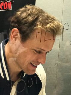 a man is smiling while looking at his cell phone with writing on the side of his head