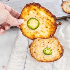 two crackers with cheese and jalapenos on them are being held up