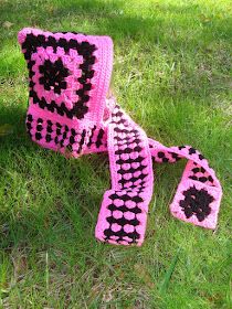 a pink and black crocheted scarf laying on the grass in front of a tree