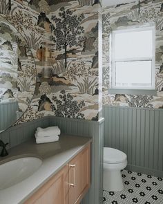 a bathroom with a toilet, sink and wall papered in animal designs on the walls