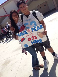 a young man and woman holding a sign in front of a building