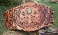 a brown leather belt with an intricate design on the front and center, sitting on top of a tree trunk