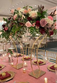 an elegant centerpiece with pink and white flowers in gold stands on top of a pink table cloth