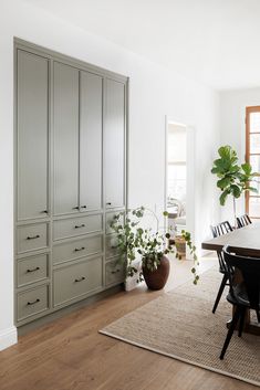 a dining room table and chairs with plants in the corner next to it on top of a rug